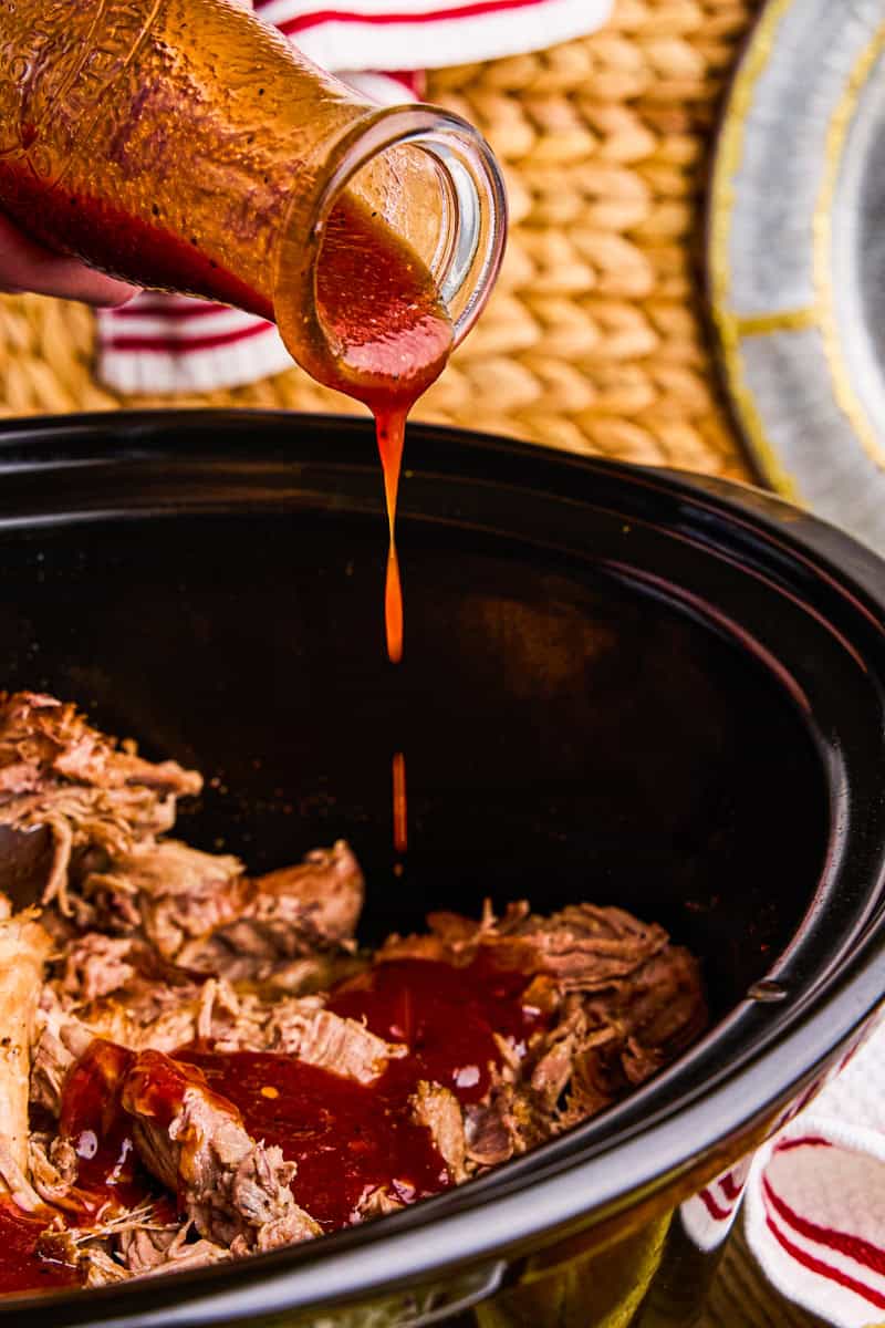 BBQ sauce being poured over Slow Cooker BBQ Pulled Pork.