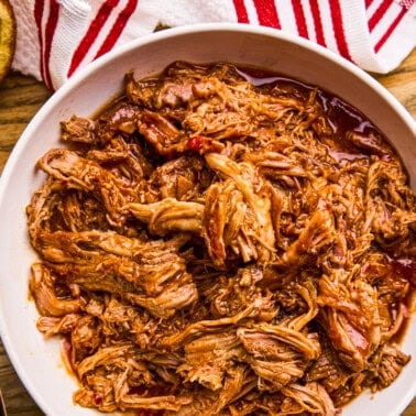 Slow Cooker BBQ Pulled Pork in a bowl with buns and coleslaw surrounding.