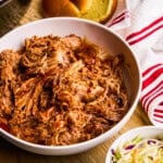 Slow Cooker BBQ Pulled Pork in a bowl with buns and coleslaw surrounding.