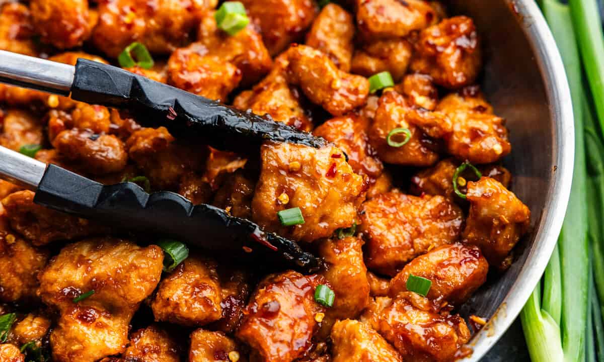 Closeup shot of General Tso Chicken on a skillet with tongs.