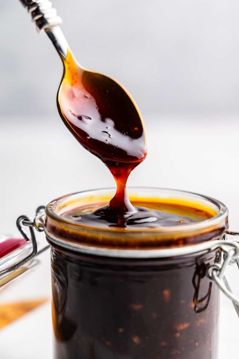 Closeup of spoon drizzling teriyaki sauce into glass.