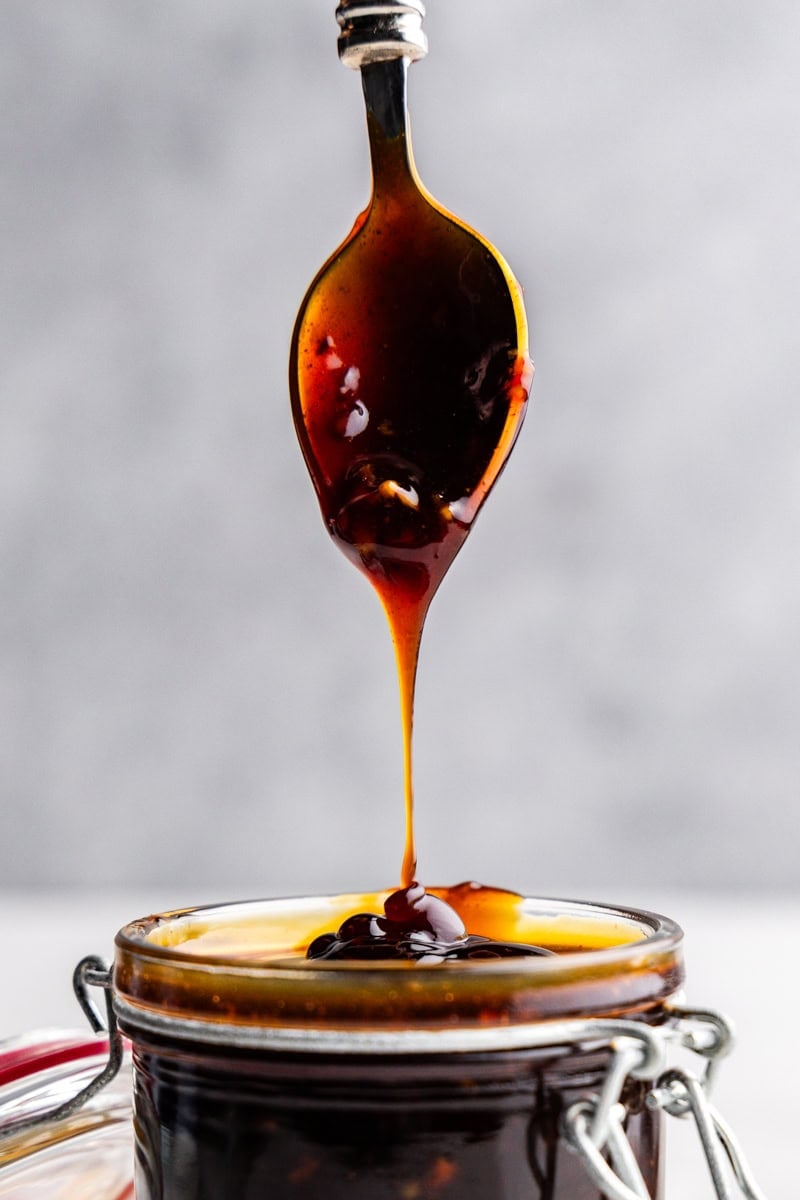 Closeup of spoon drizzling teriyaki sauce into glass.