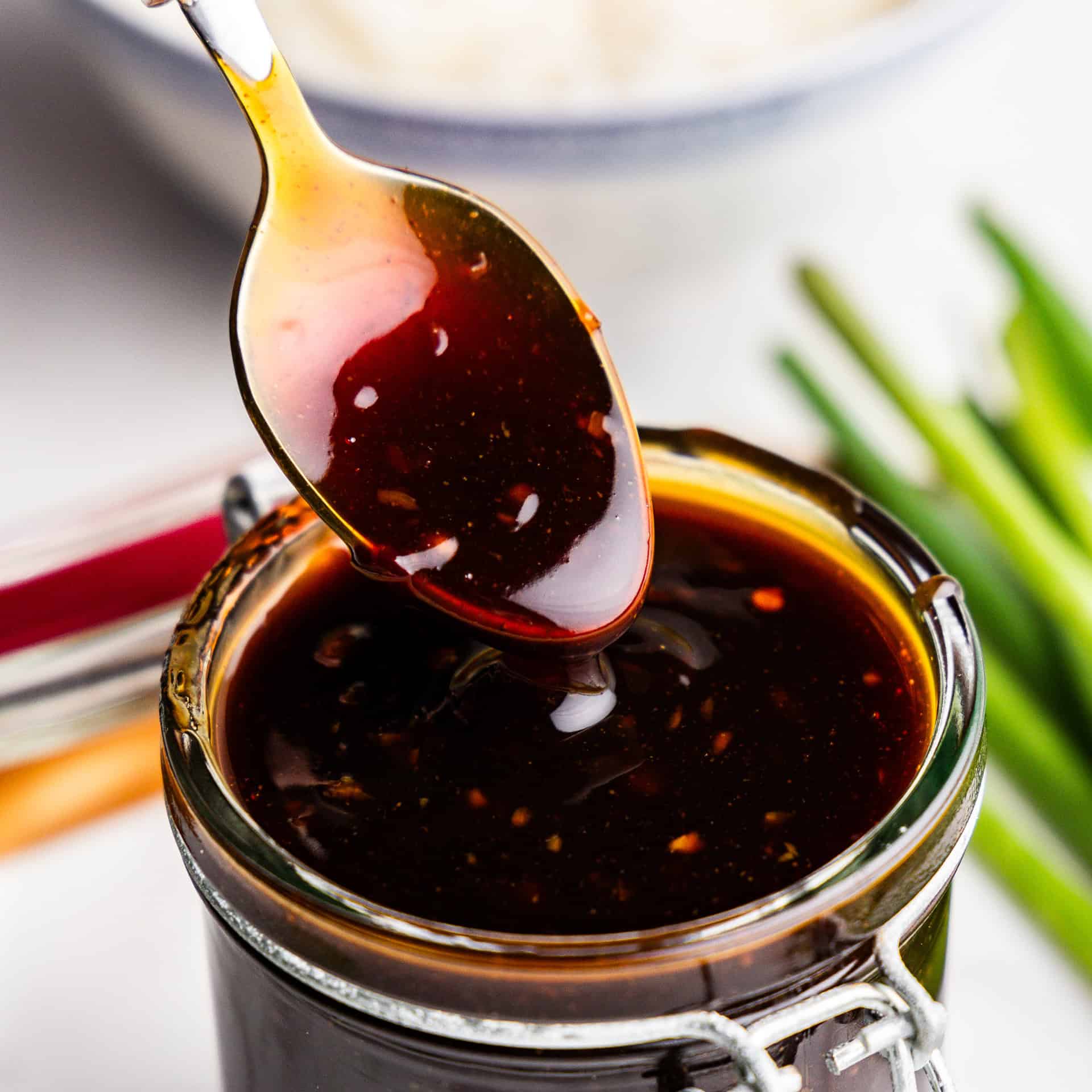 Closeup of teriyaki sauce being lifted with spoon out of glass.