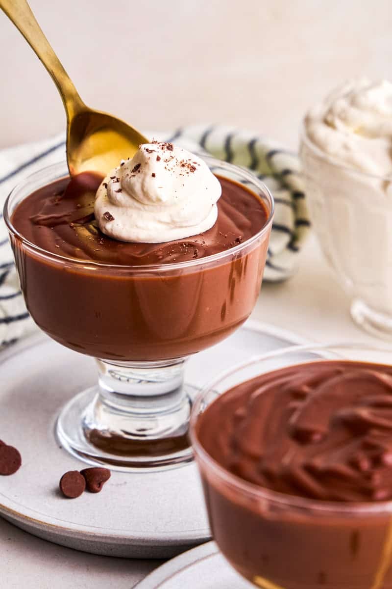 A spoon taking a scoop of 5 Ingredient Homemade Chocolate Pudding with whip cream and chocolate shavings.