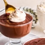 A spoon taking a scoop of 5 Ingredient Homemade Chocolate Pudding with whip cream and chocolate shavings.