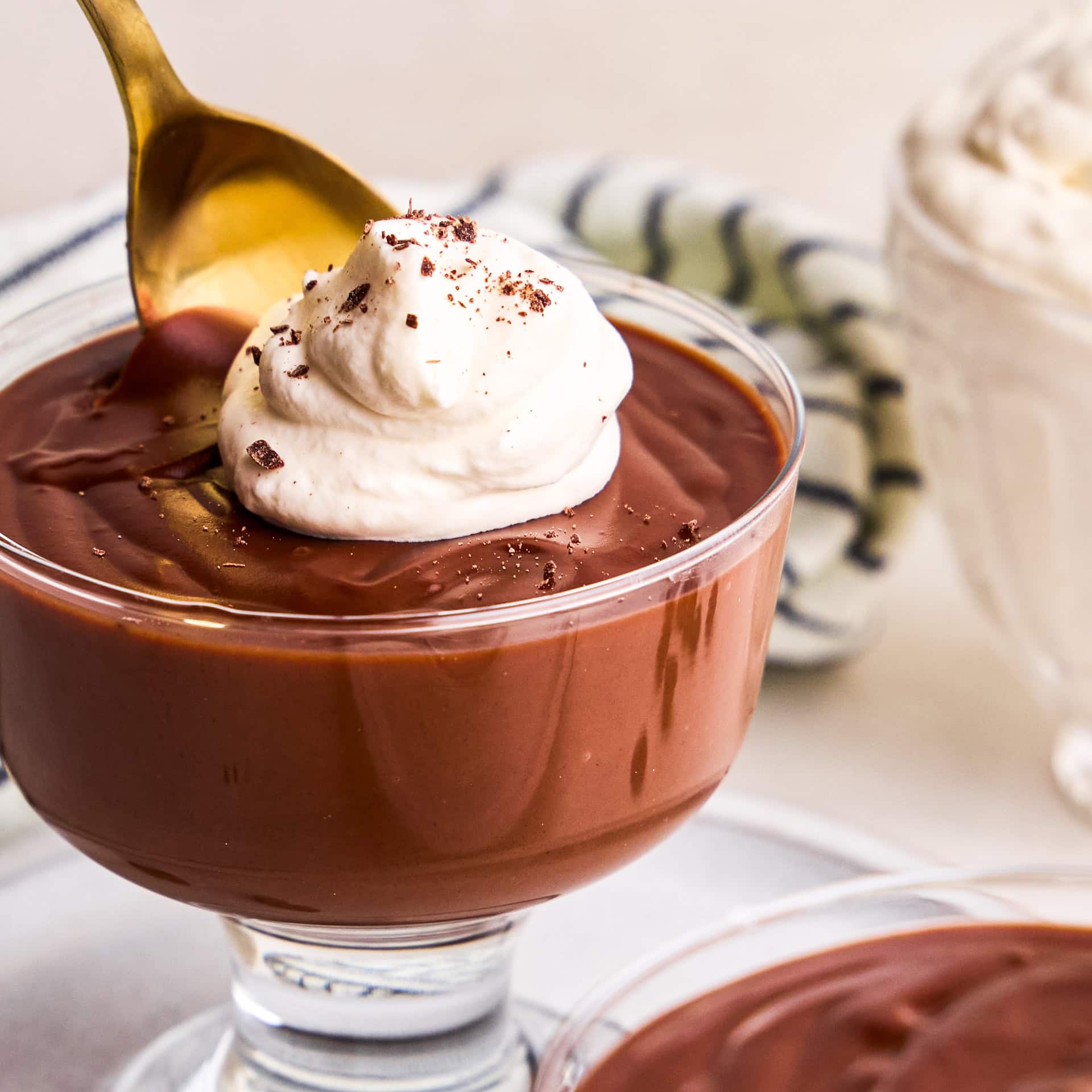 A spoon taking a scoop of 5 Ingredient Homemade Chocolate Pudding with whip cream and chocolate shavings.