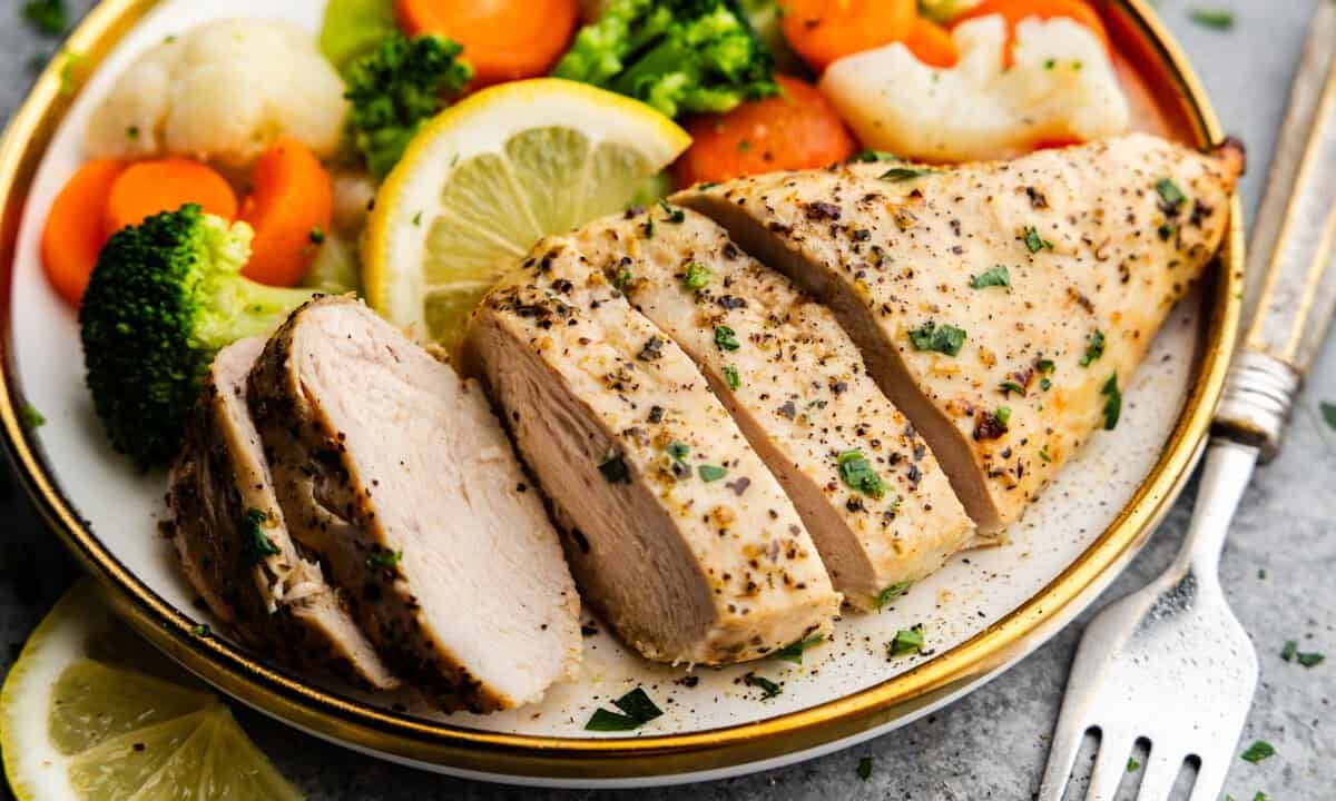 Closeup of Chicken breast sliced on a plate with veggies and lemons.