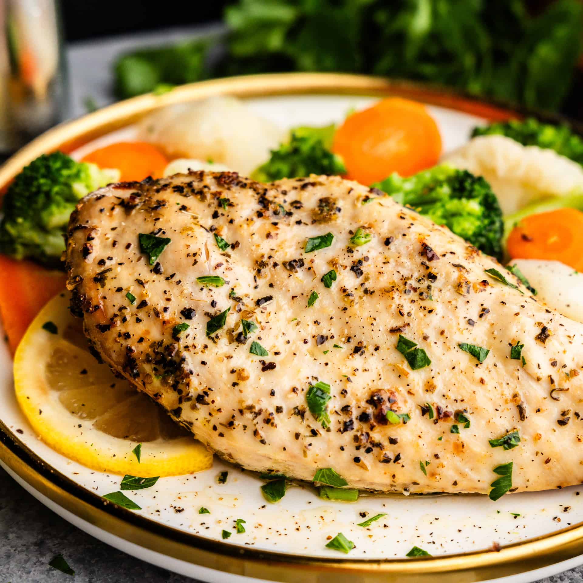 Closeup of Chicken breast on a plate with veggies and lemons.