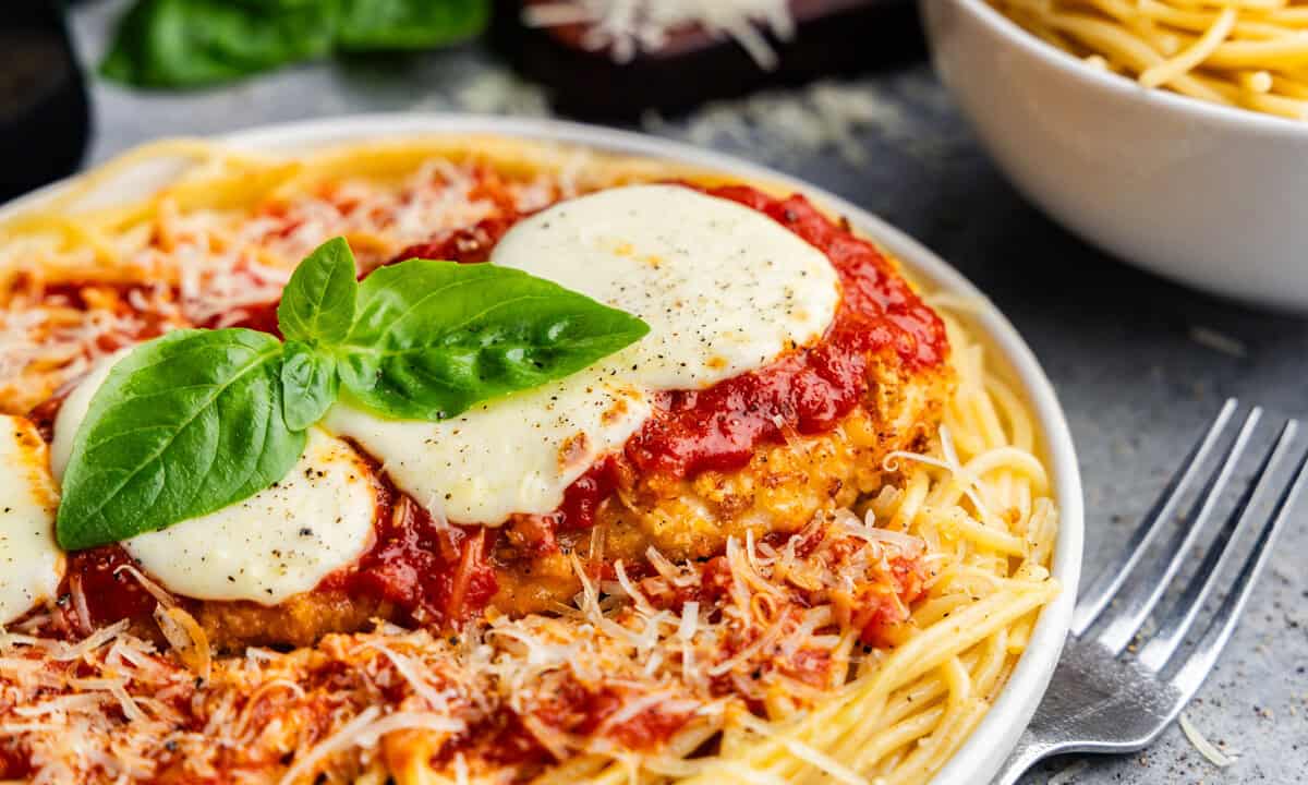 Closeup of chicken parmesan on a plate of pasta.