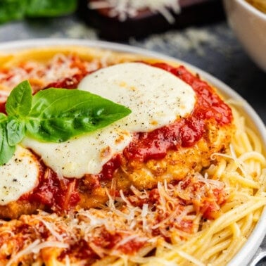 Closeup of chicken parmesan on a plate of pasta.