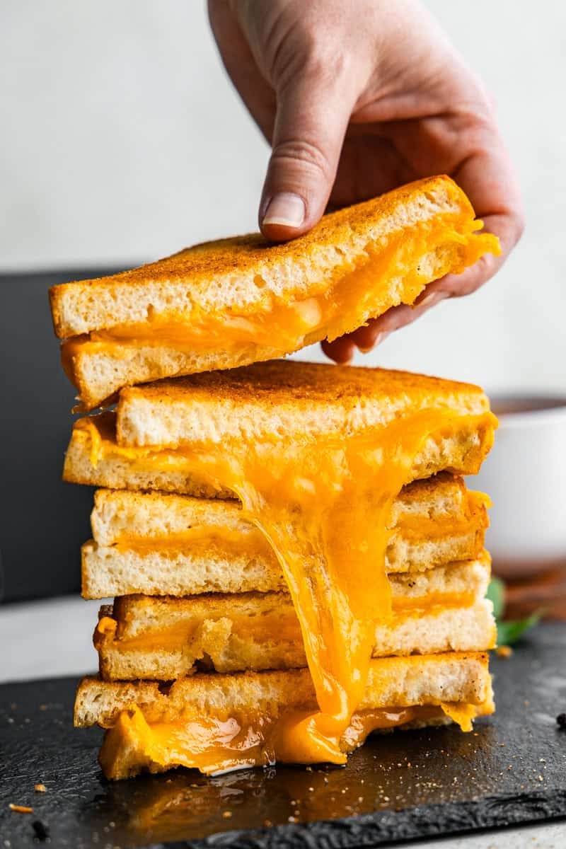 Pile of split in half Grilled cheese sandwiches in front of an air fryer.