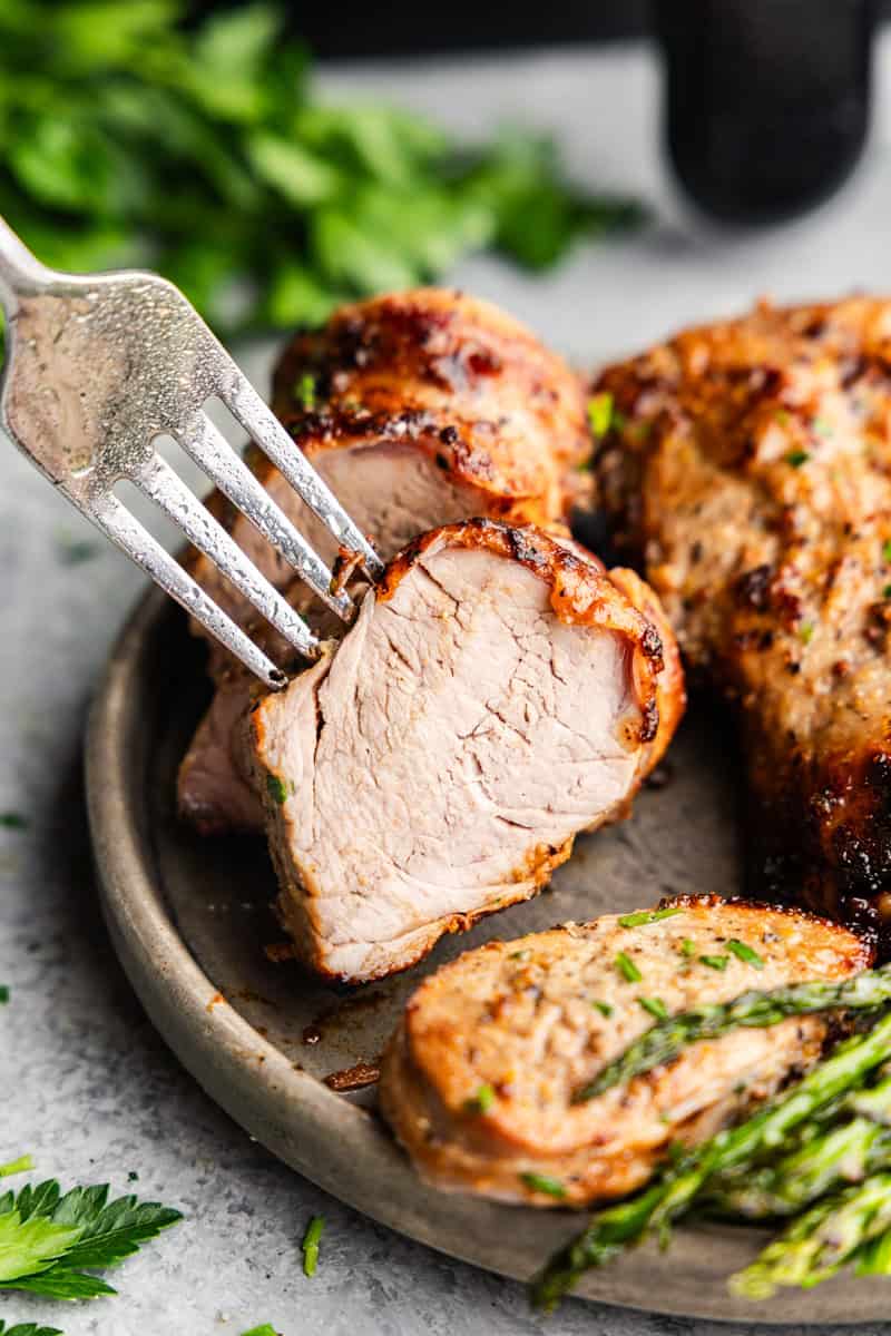 Closeup of fork bite of Pork tenderloin on a plate with asparagus.