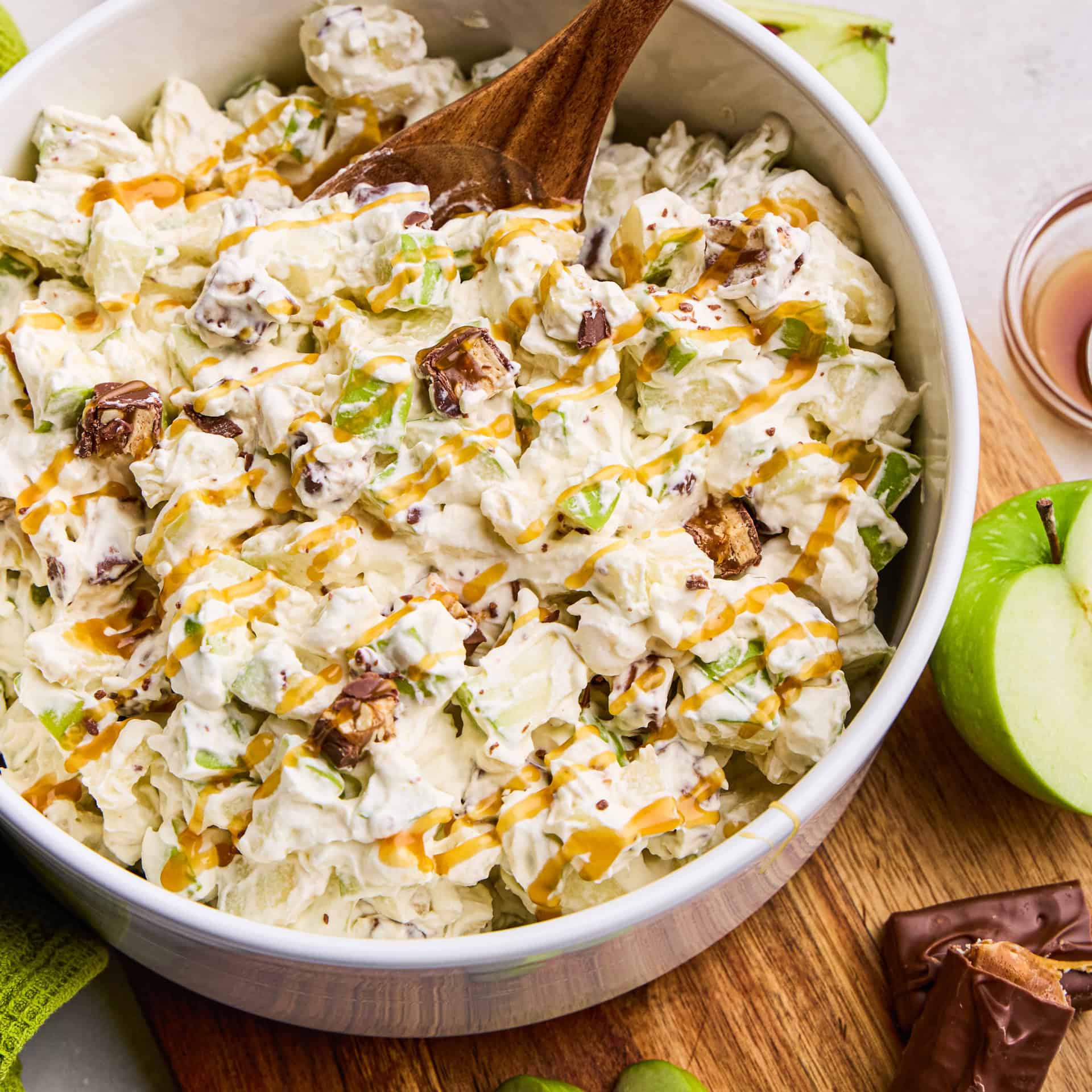 Apple Snickers Salad in a bowl with wooden spoon.