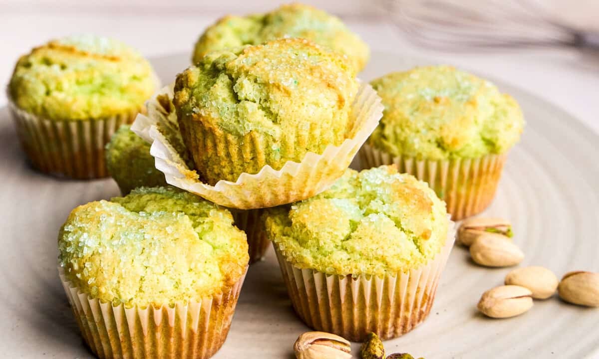Bakery Style Pistachio Muffins stacked on top of each other on a display stand with pistachios laying next to them.