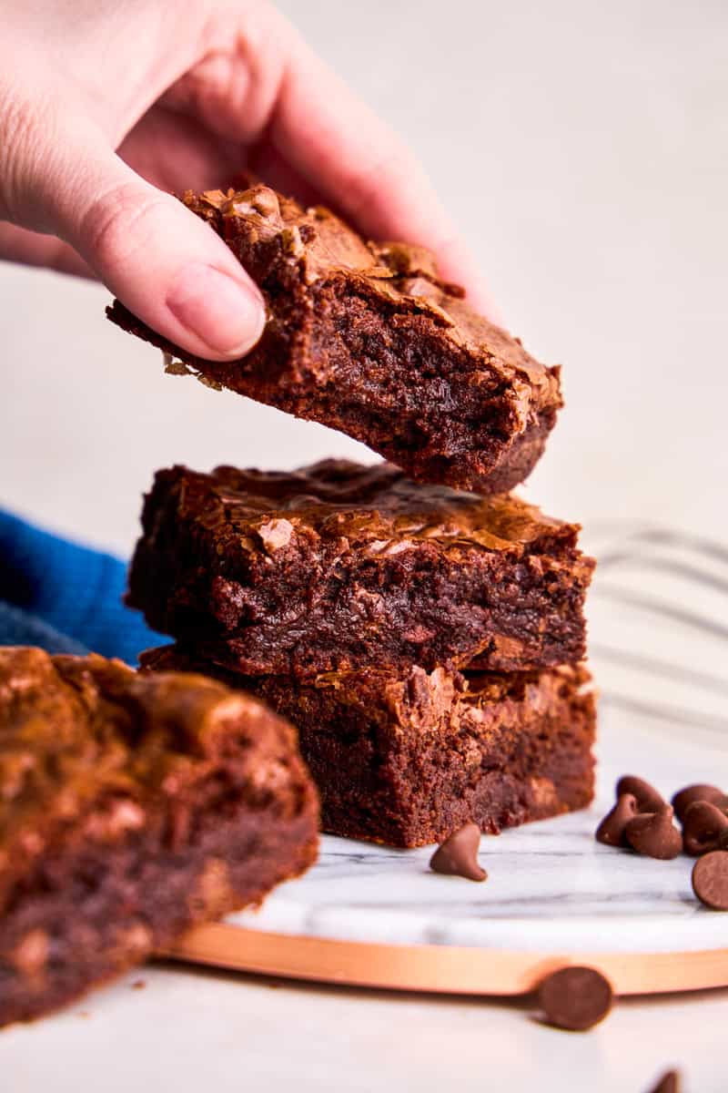 A hand placing a brownie with a bite out of it onto a stack brownies from The Best Brownie Recipe Ever.