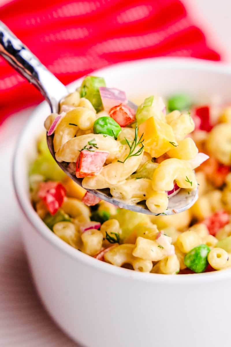 A spoonful of the Best Macaroni Salad hovering above a white bowl.