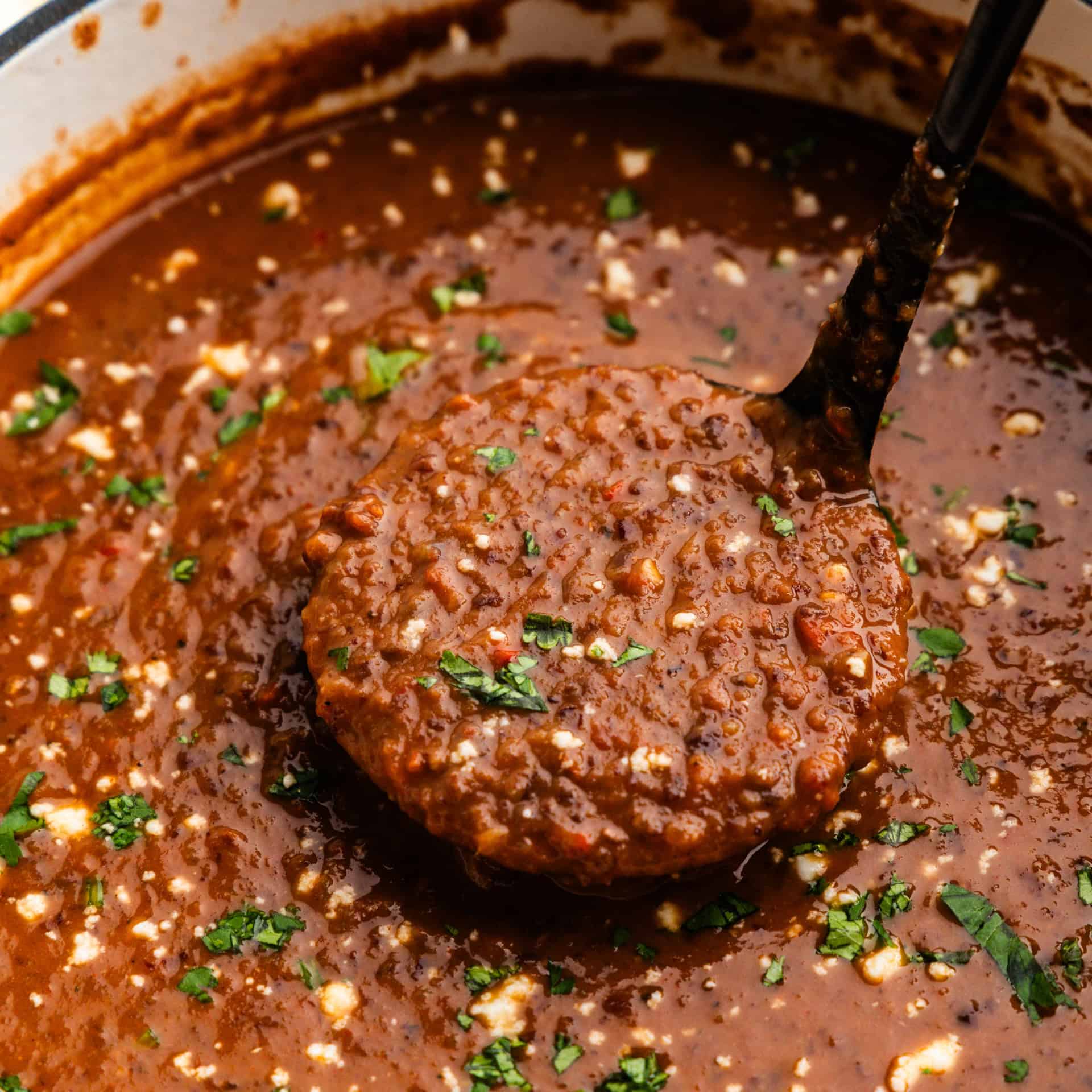 Closeup of a ladleful of Black Bean Soup in a pot.