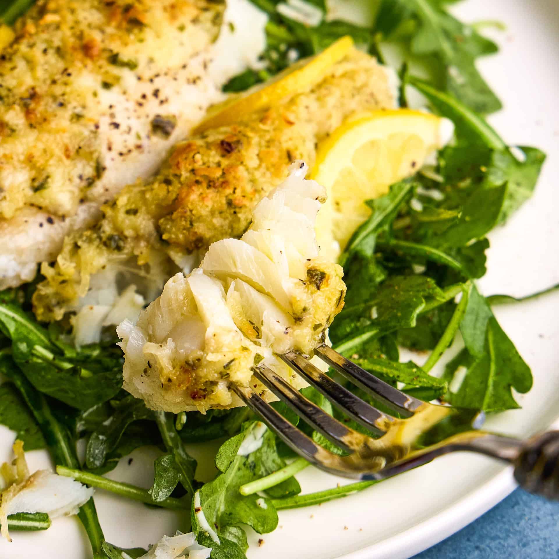 A bite of Easy Lemon Baked Cod Fish on a fork near a plated dish.