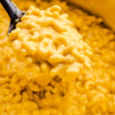 A serving spoon loaded with Easy Stovetop Mac and Cheese hovering over a cast iron pot full of Mac and Cheese.
