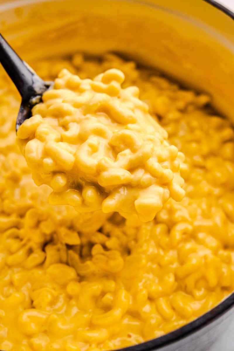 A serving spoon loaded with Easy Stovetop Mac and Cheese hovering over a cast iron pot full of Mac and Cheese.