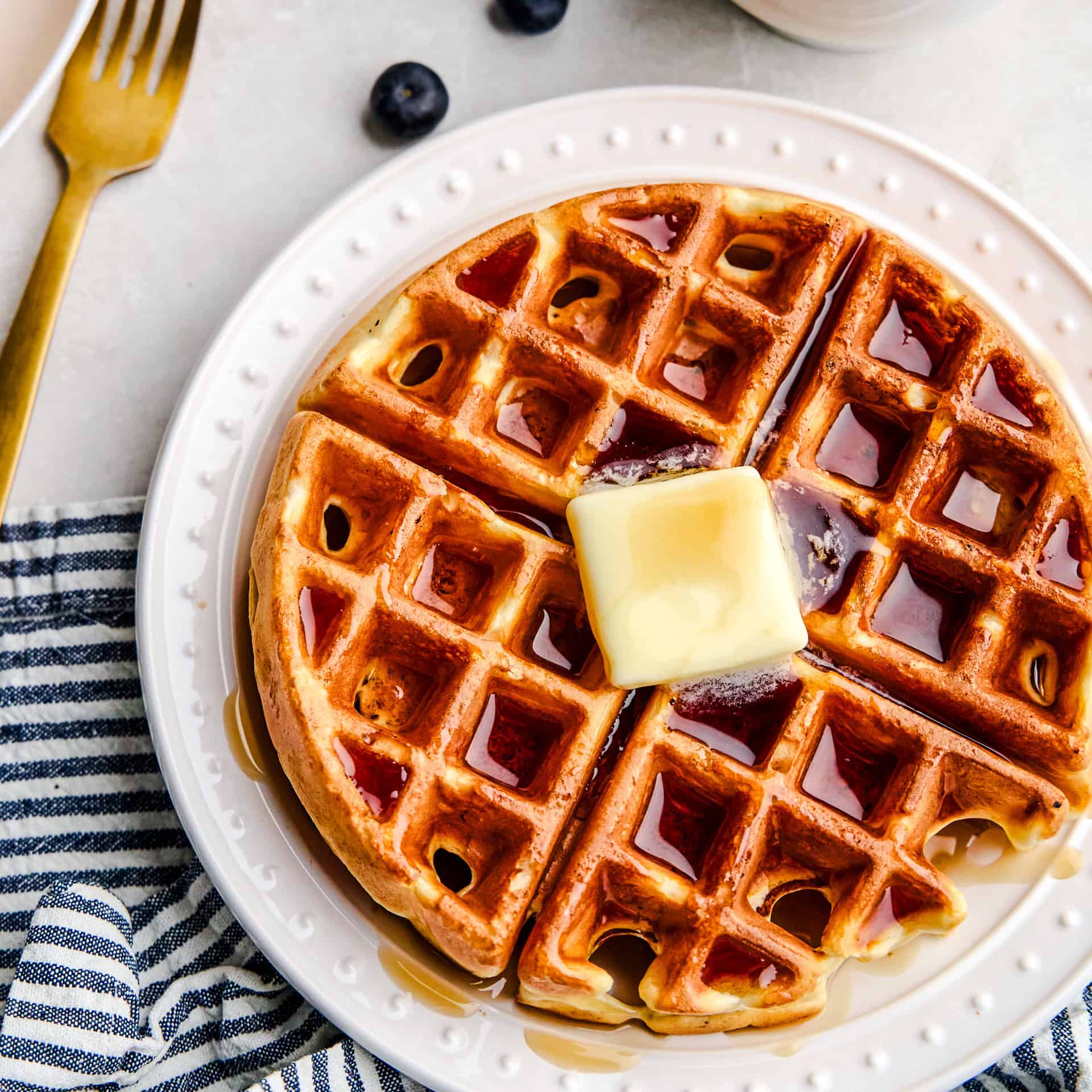 An overhead image of a Greek Yogurt Waffle with a pat of butter and syrup drizzled over top.
