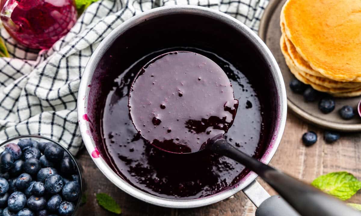 Pot of blueberry syrup with a ladleful in it.