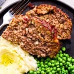 Two Slices of Momma's Meatloaf on a plate with mashed potatoes and green peas.