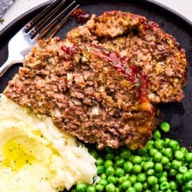 Two Slices of Momma's Meatloaf on a plate with mashed potatoes and green peas.