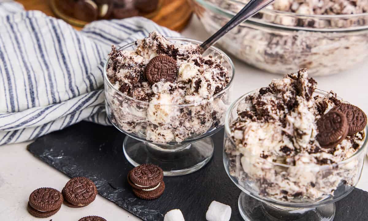 Oreo Fluff in a parfait cup with spoon in it and marshmallows and chocolate sandwich cookies scattered around.