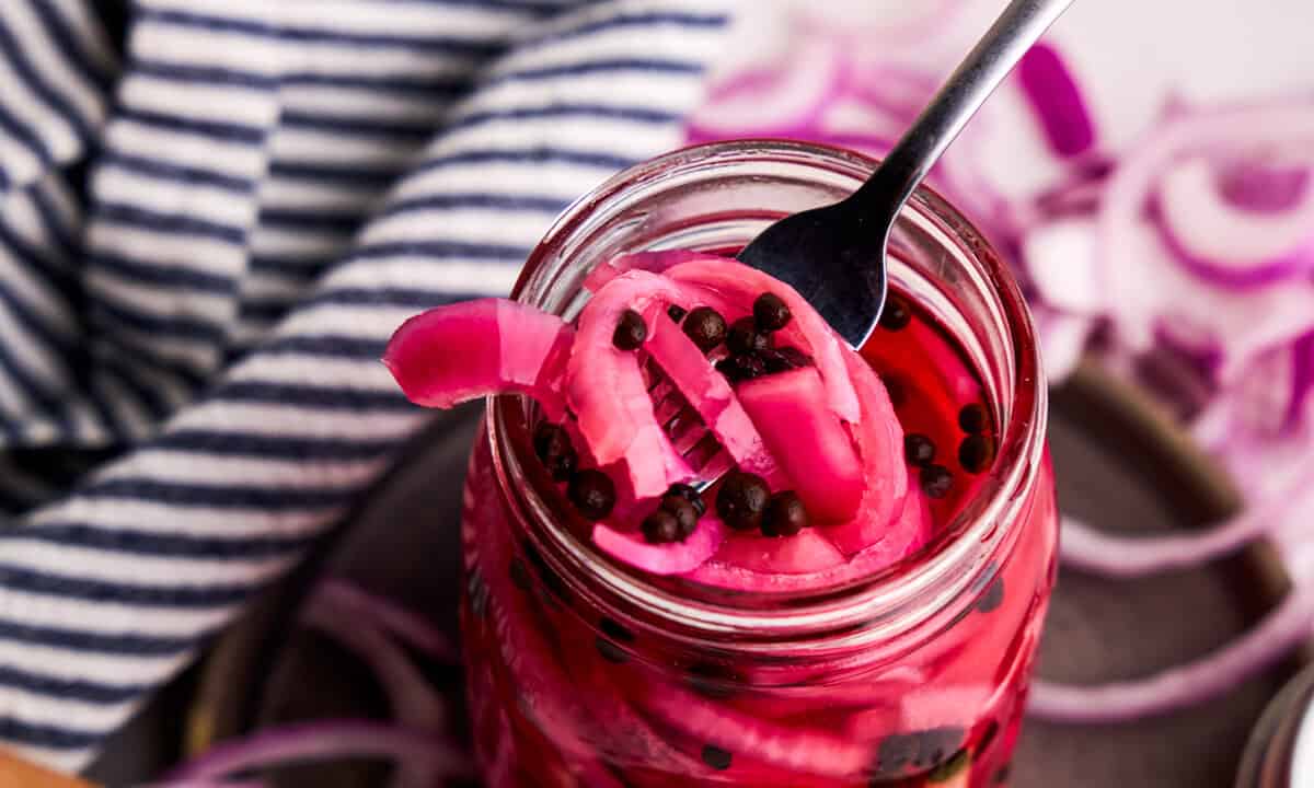 A forkful of Pickled Red Onions being lifted from a glass jar.