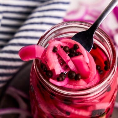 A forkful of Pickled Red Onions being lifted from a glass jar.