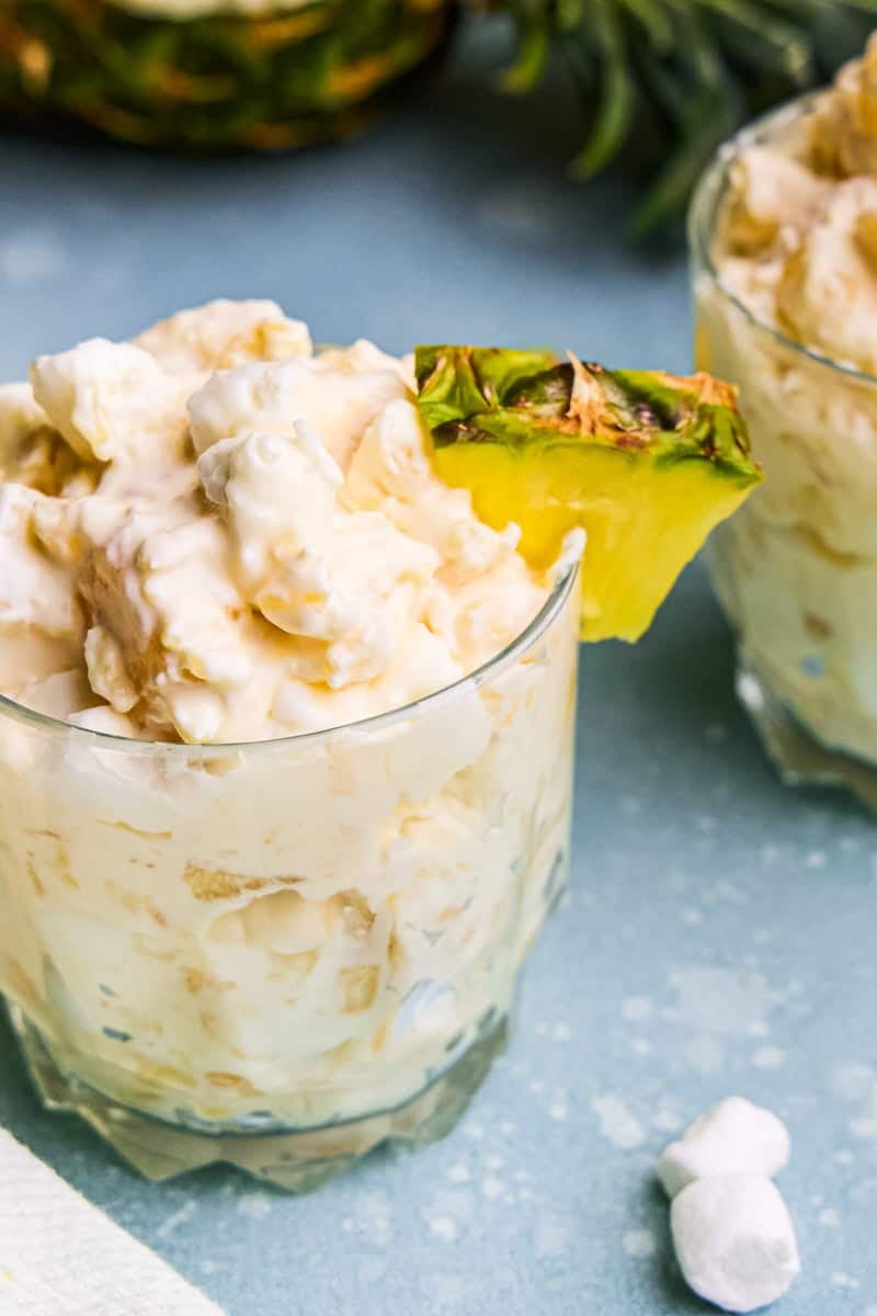 Pineapple Fluff in a glass cup with pineapple chunk on the rim.