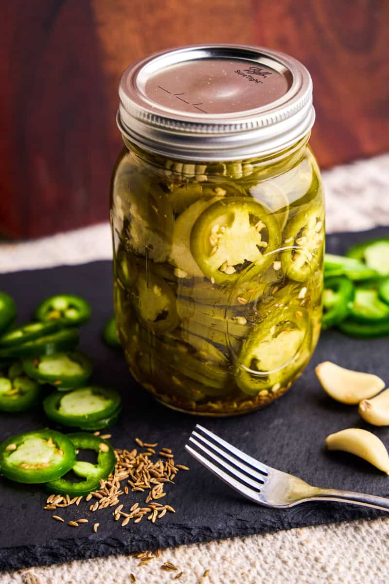 A Jar of Quick Pickled Jalapeños with fresh ingredients laying near.