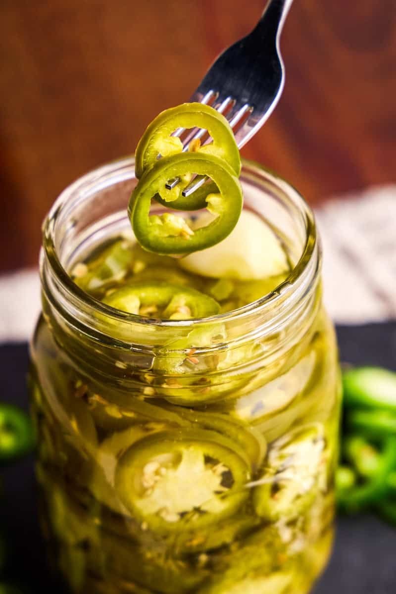 A fork holding two jalapeño slices above a jar of Quick Pickled Jalapeños.