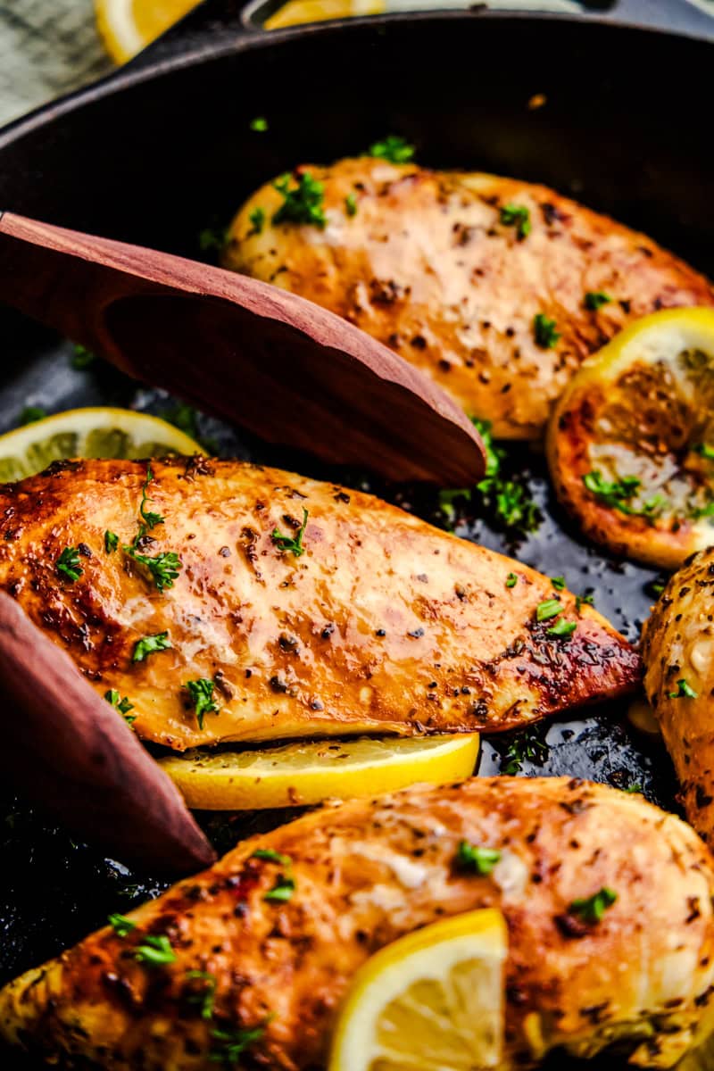 Tongs grabbing a piece of Quick and Easy Lemon Chicken out of a dark cast iron pan.