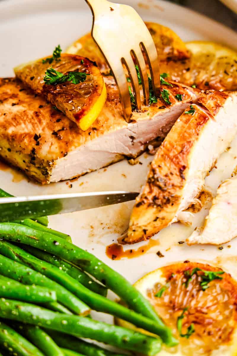 A fork and knife slicing into Quick and Easy Lemon Chicken on a plate with a side of green beans.
