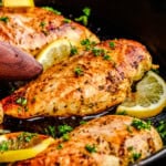 A closeup image of Quick and Easy Lemon Chicken in a dark cast iron pan and garnished with fresh parsley and lemon slices.