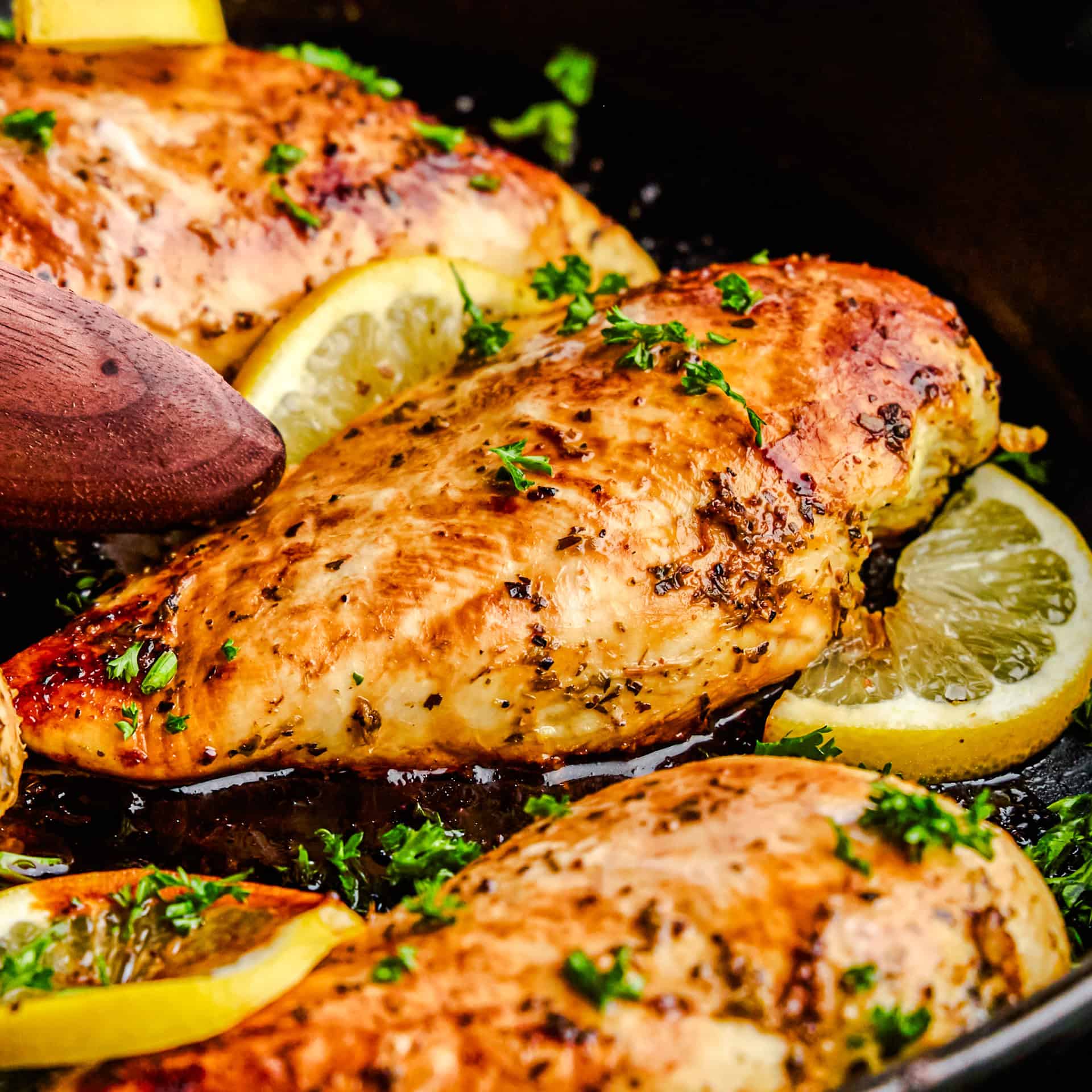 A closeup image of Quick and Easy Lemon Chicken in a dark cast iron pan and garnished with fresh parsley and lemon slices.