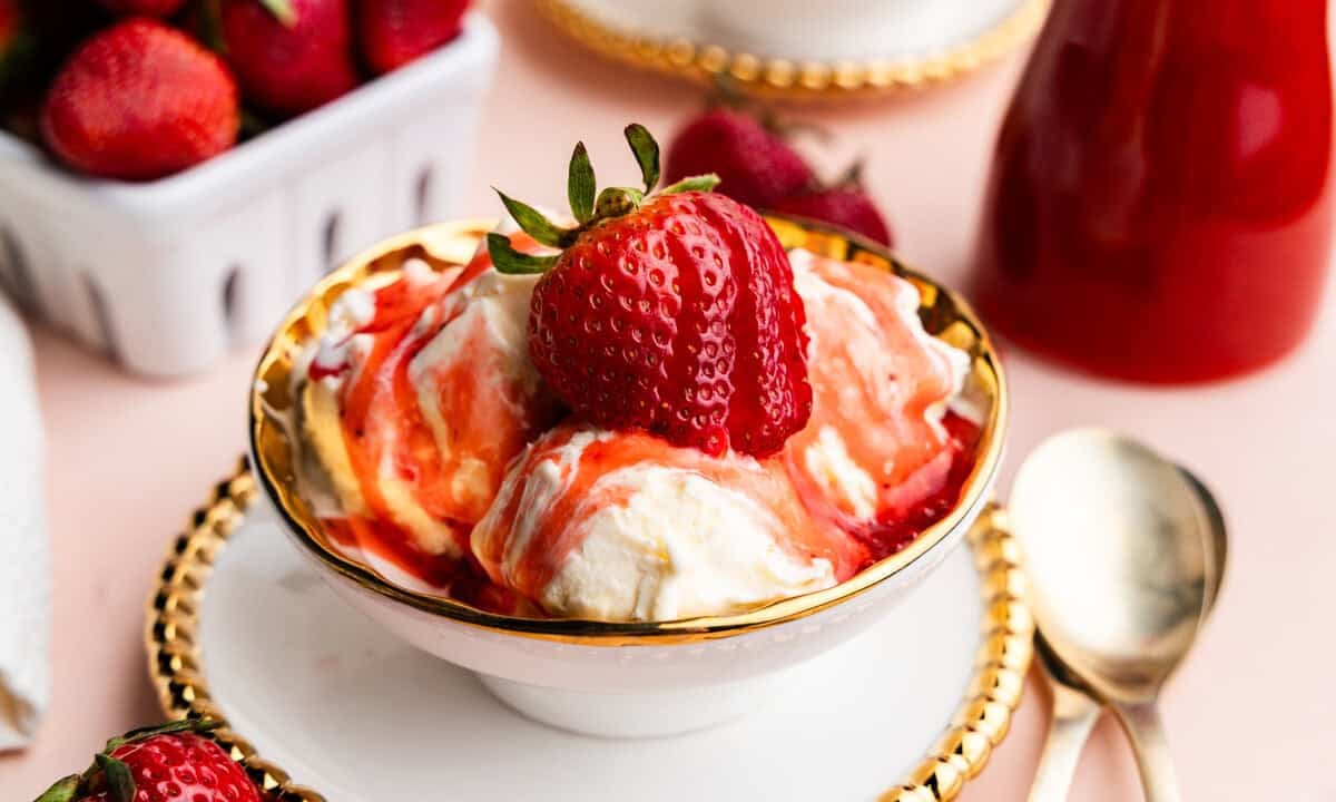Bowl of ice cream with strawberry syrup on top with a strawberry in the middle.
