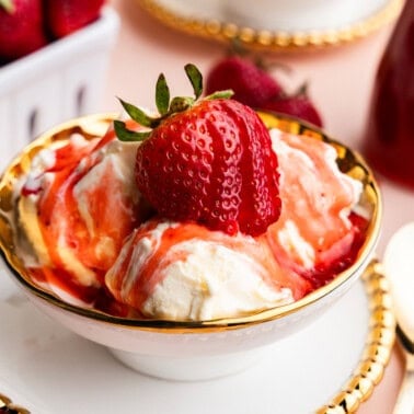 Bowl of ice cream with strawberry syrup on top with a strawberry in the middle.
