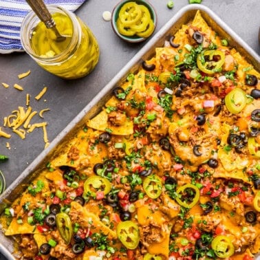 Overhead image of a pan of Ultimate Nacho Recipe with ingredients and toppings surrounding it.