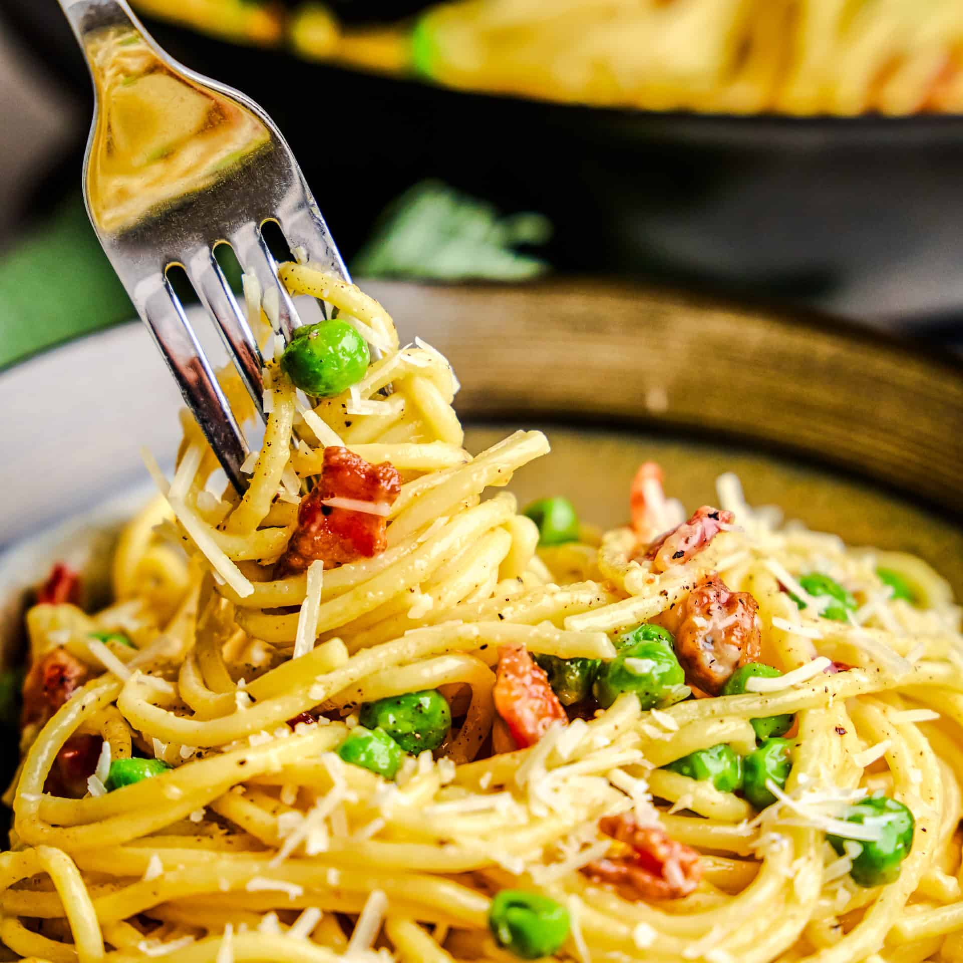 A forkful of American Carbonara in a bowl topped with fresh grated parmesan cheese.
