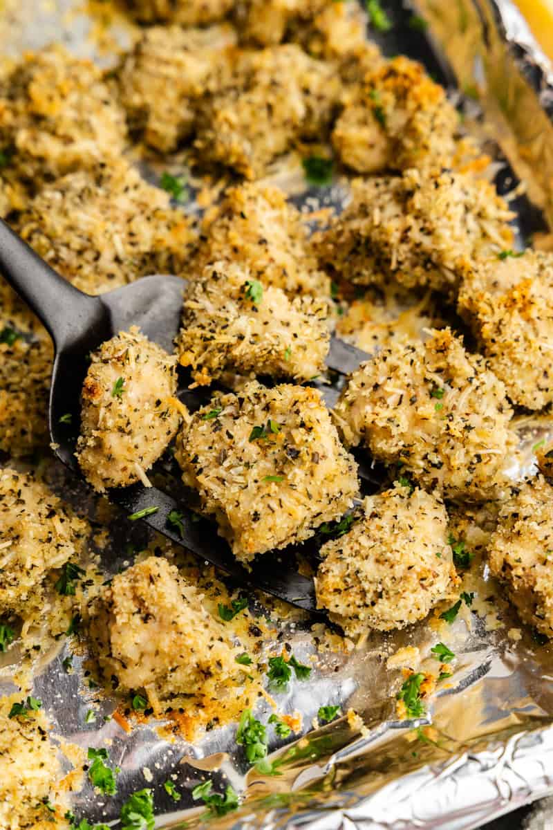Chicken nuggets being scooped with a spatula from baking tray.