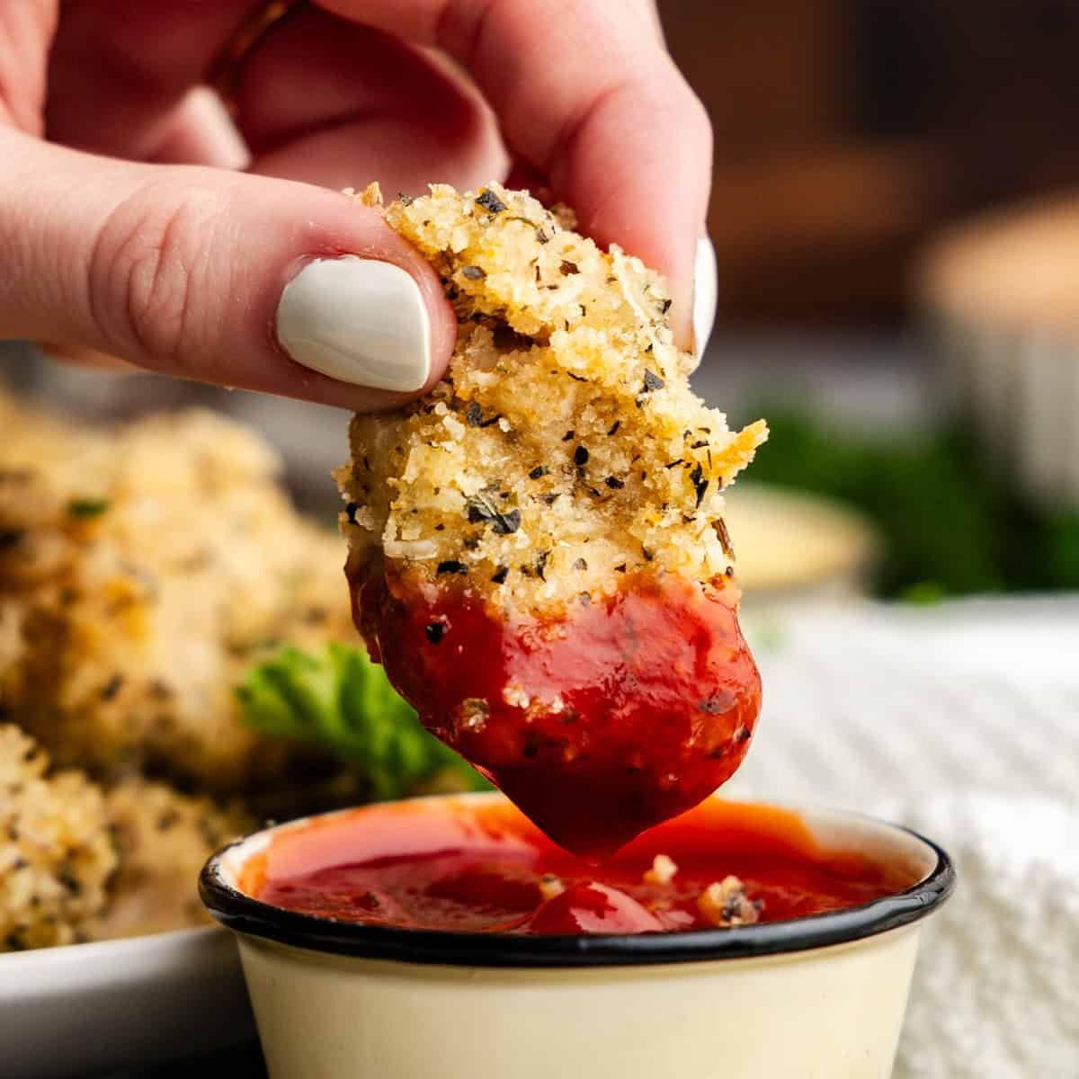 Closeup of chicken nugget being dipped in ketchup.