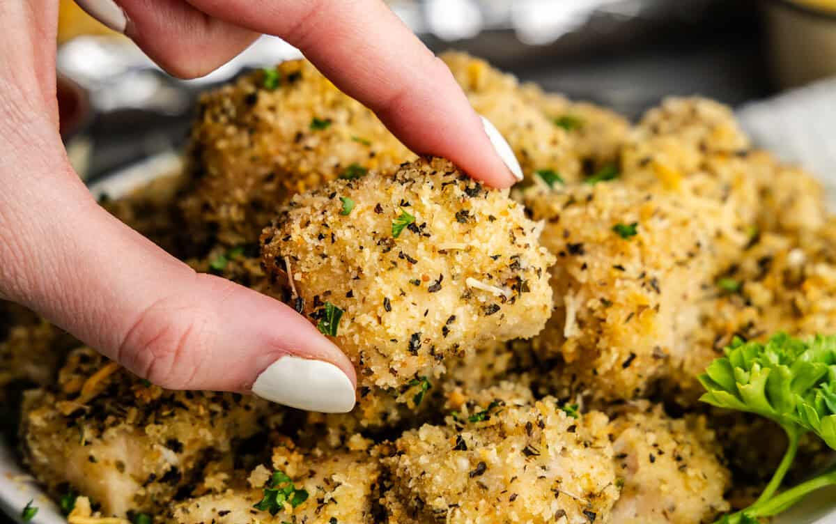Closeup of chicken nugget being picked up over a plate of chicken nuggets.