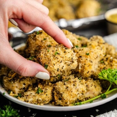 Closeup of chicken nugget being picked up over a plate of chicken nuggets.