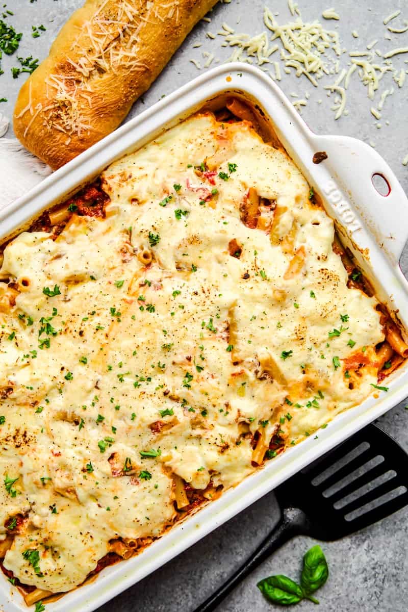 An overhead image of The Best Baked Ziti Ever in a baking dish with sprinkled cheese and a baguette.