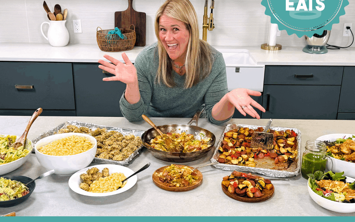 A photo of Chef Cayt in The Stay At Home Chef Kitchen with the meals from Week 2 of the Cheap Eats Meal plan on display on the kitchen counter.