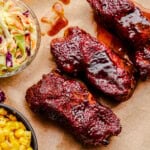 Country Style Pork Ribs on parchment paper with coleslaw and corn next to them.