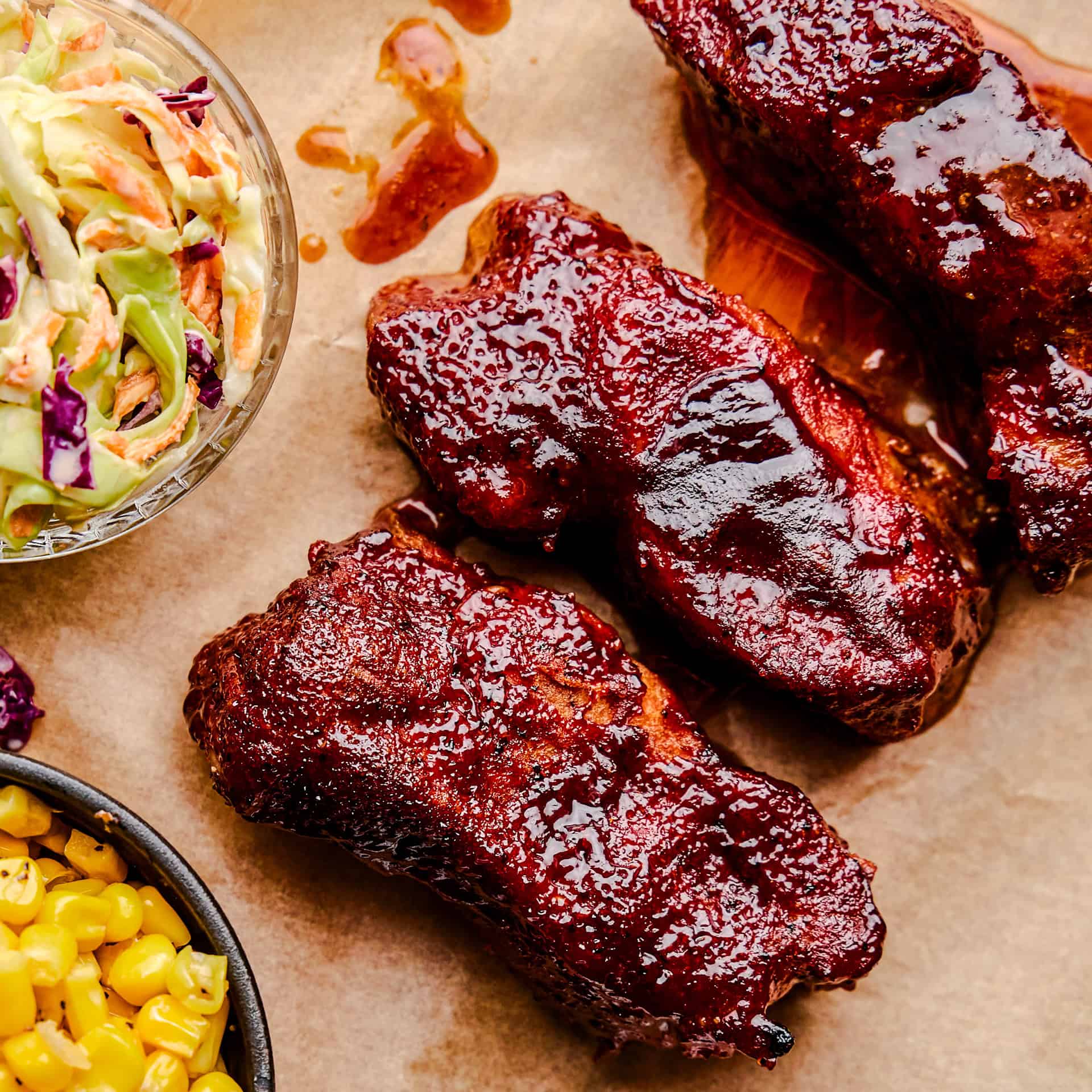 Country Style Pork Ribs on parchment paper with coleslaw and corn next to them.